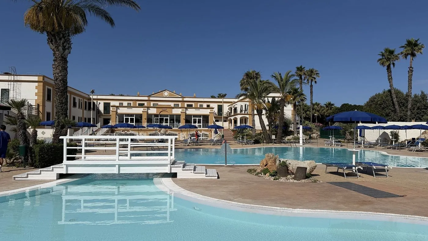 Piscina con ponte bianco e lettini davanti all'edificio dell'hotel