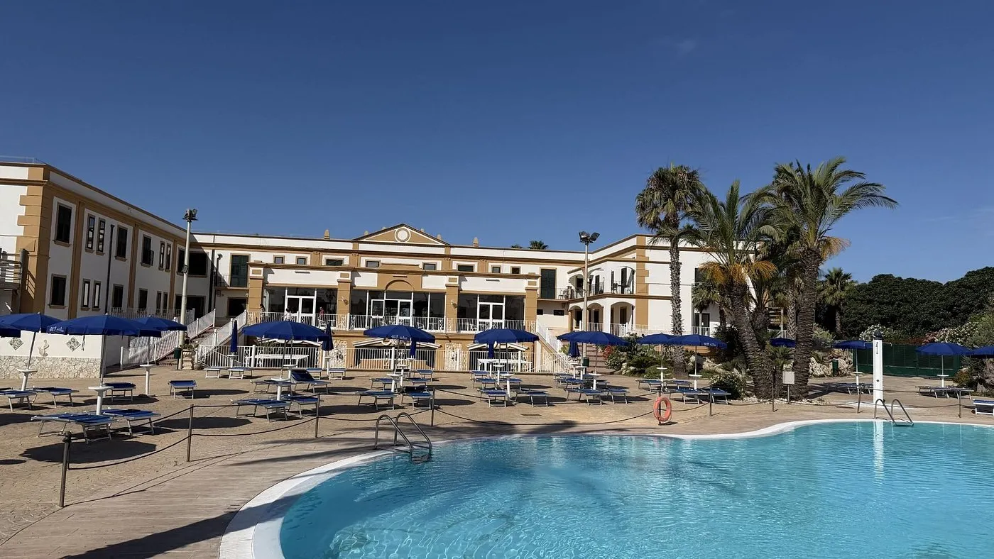 Piscina con lettini e ombrelloni blu davanti alla facciata dell'hotel