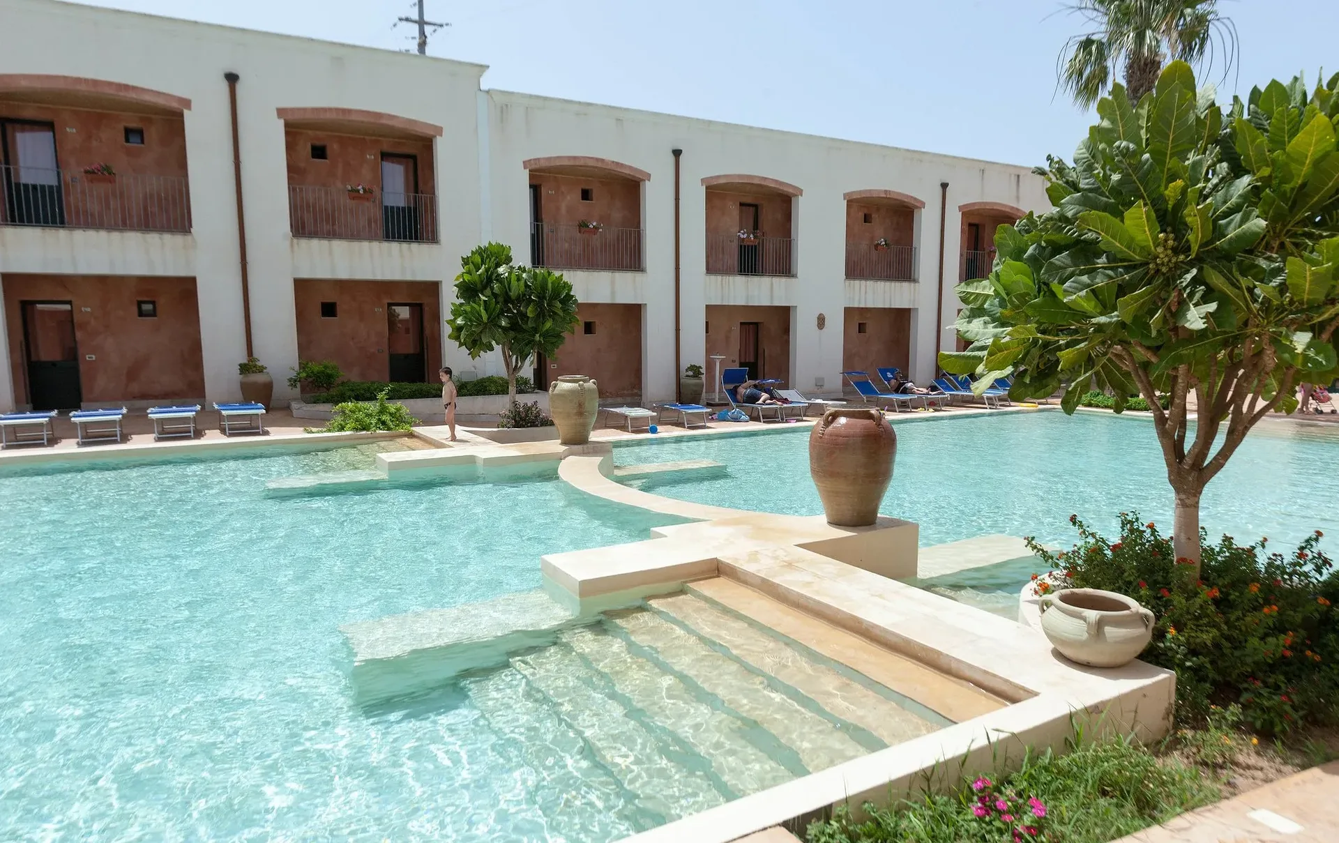 Piscina con gradini e anfore in terracotta circondata da edifici con archi