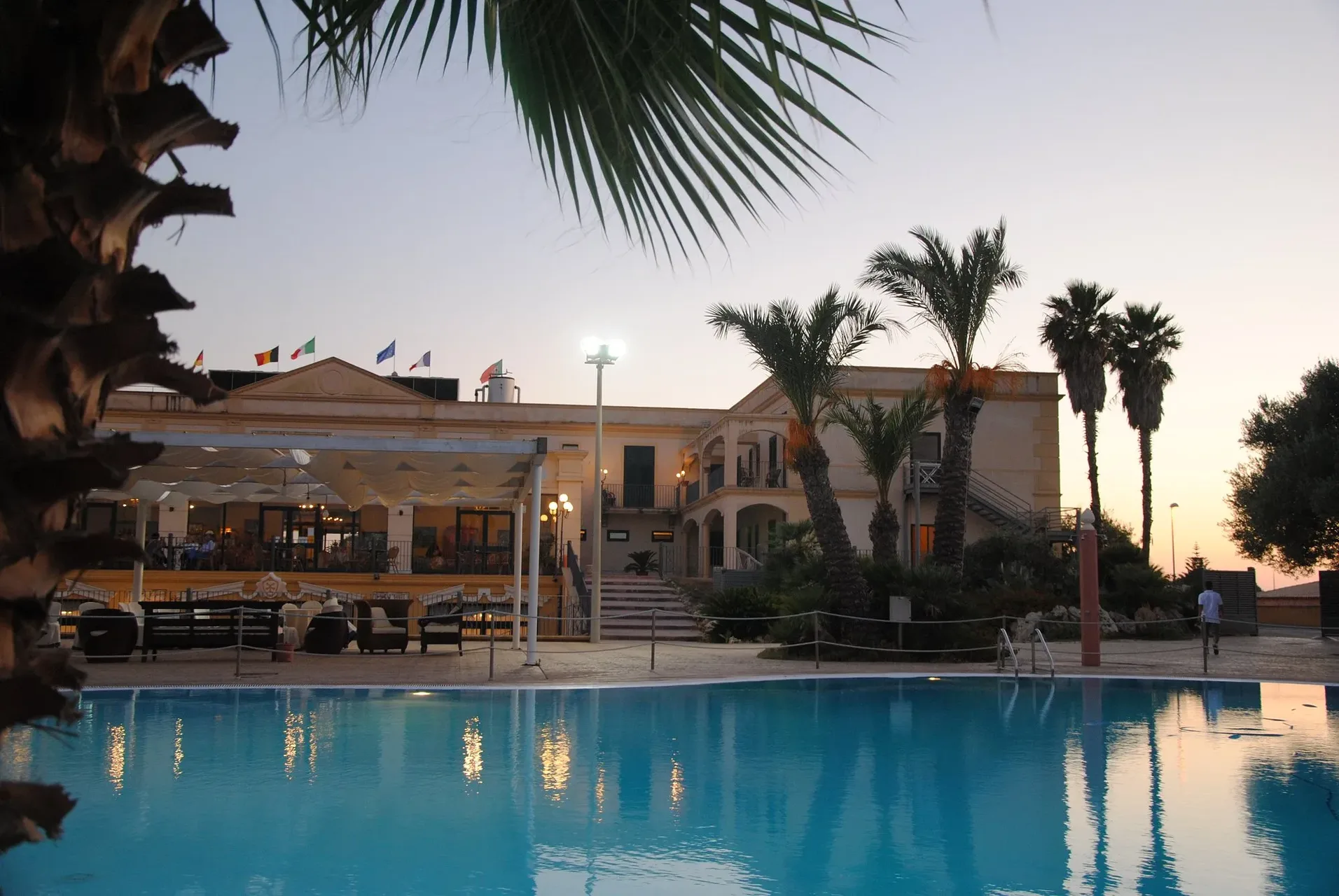 Piscina illuminata al tramonto con edificio dell'hotel e palme sullo sfondo