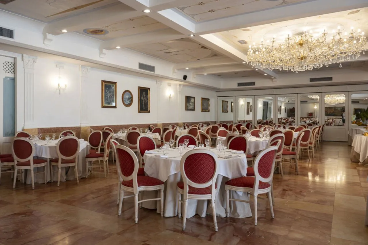 Sala ristorante elegante con tavoli rotondi, sedie rosse e lampadario di cristallo