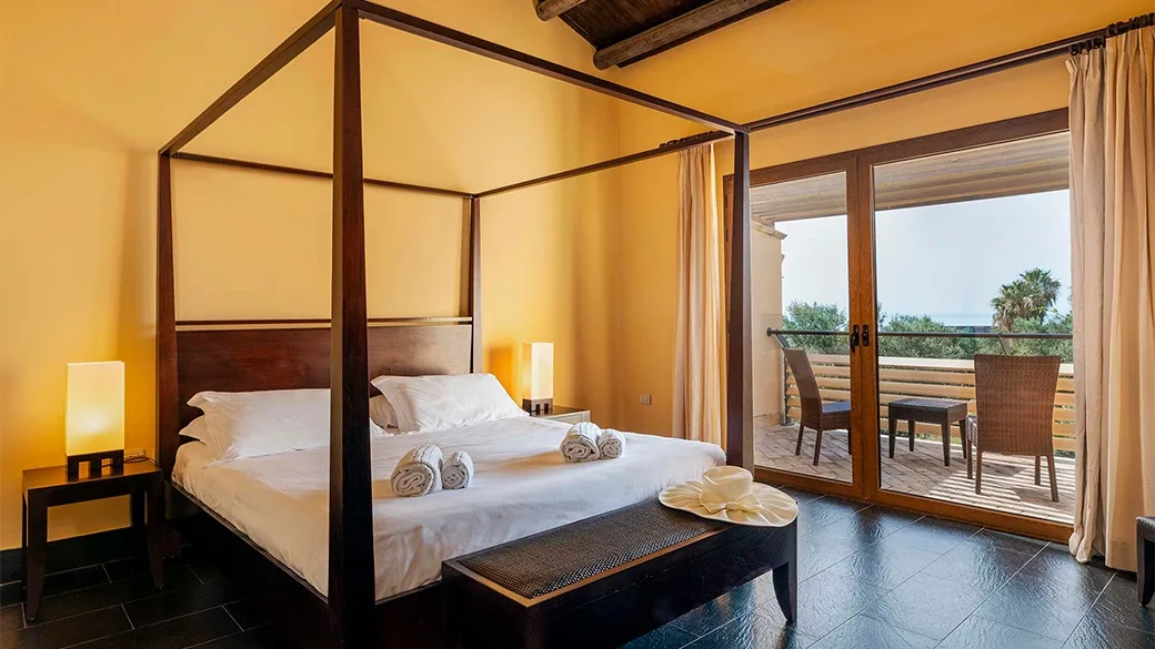 Camera con letto a baldacchino in legno scuro e balcone con vista mare
