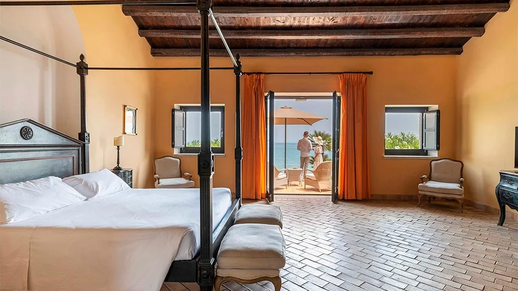 Suite con letto a baldacchino, pavimento in cotto e porta-finestra affacciata sul mare