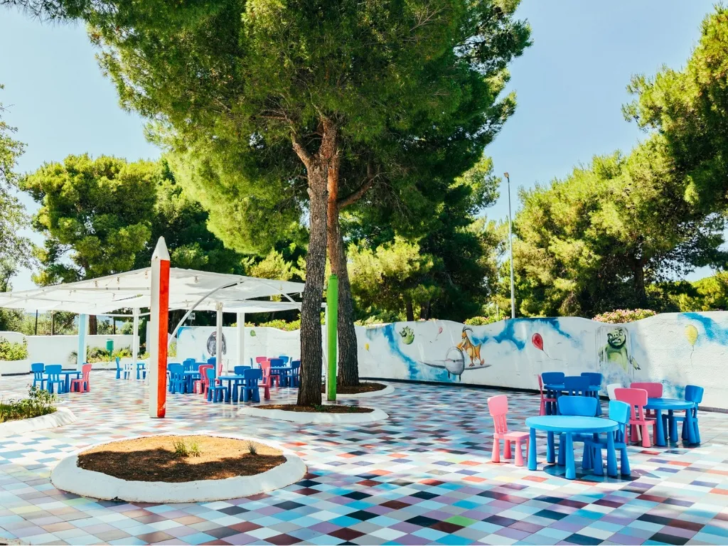 Area ristoro per bambini con tavolini e sedie colorate su pavimento a mosaico