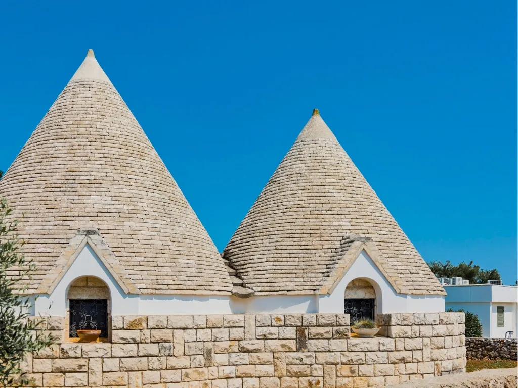 Trulli tradizionali in pietra con tetti conici sotto un cielo azzurro