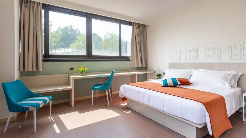 Camera luminosa con letto matrimoniale, scrivania e sedie azzurre affacciata sul verde