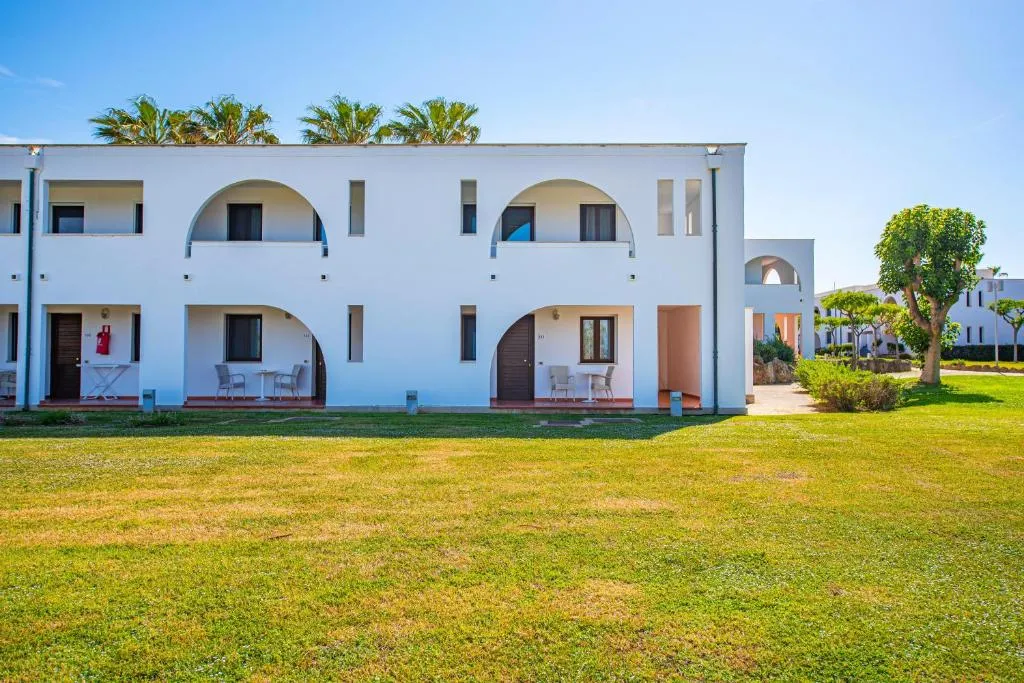 Edificio bianco ad archi con camere al piano terra e prato verde