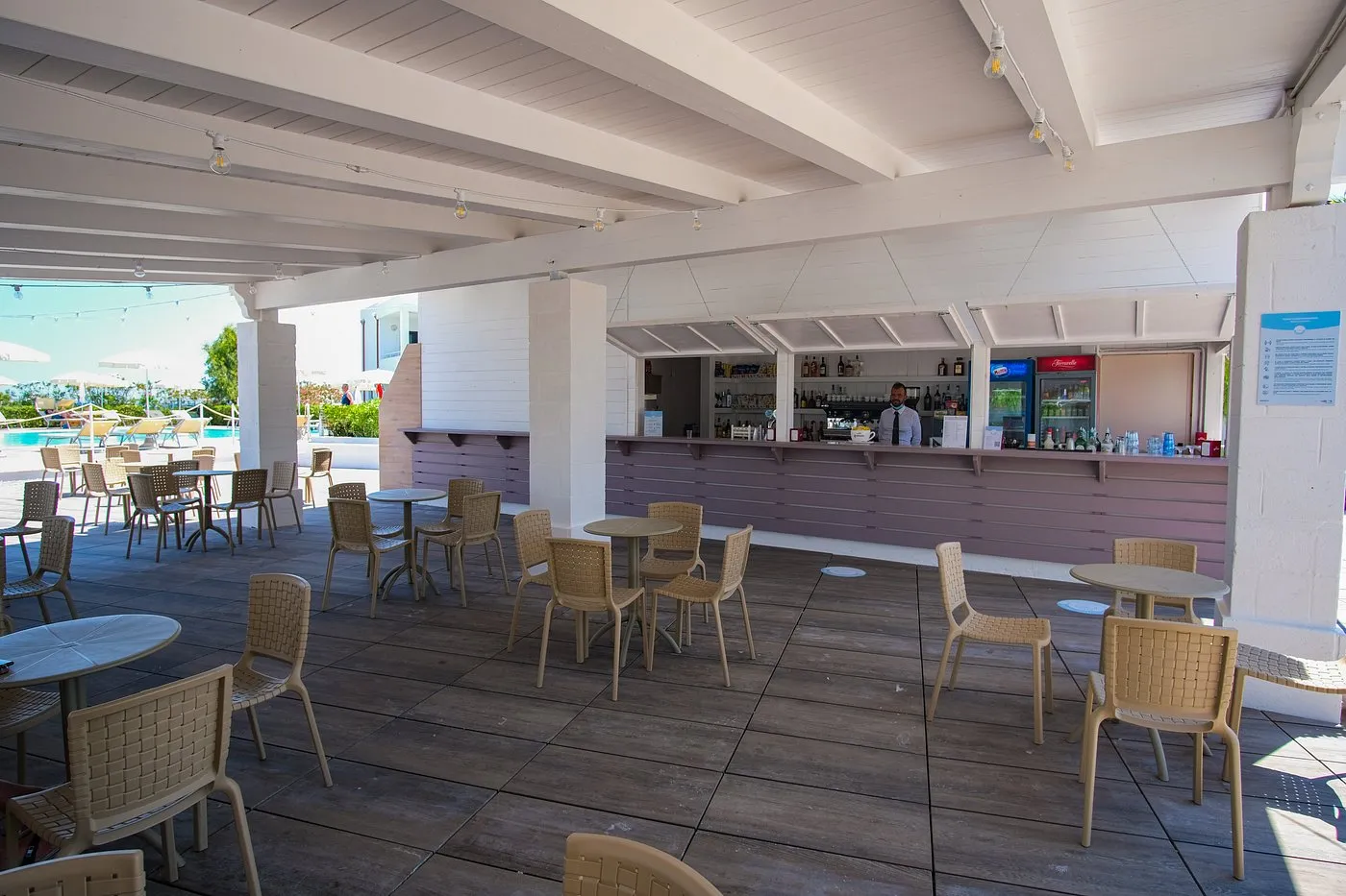 Bar esterno coperto con tavoli, sedie e barista a bordo piscina