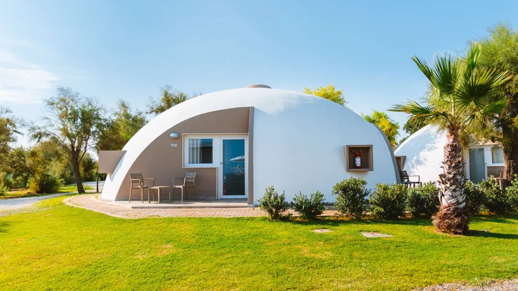 Bungalow a cupola bianco con terrazzo, tavolino e palma sul prato verde