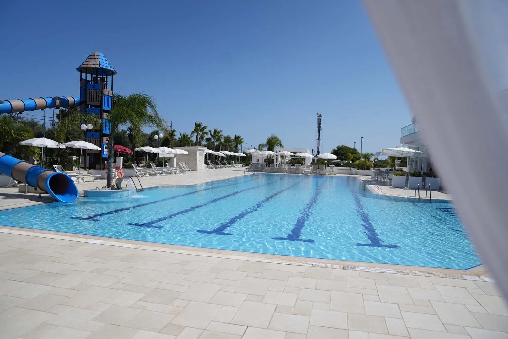 Ampia piscina con corsie, scivolo acquatico e area lettini pavimentata