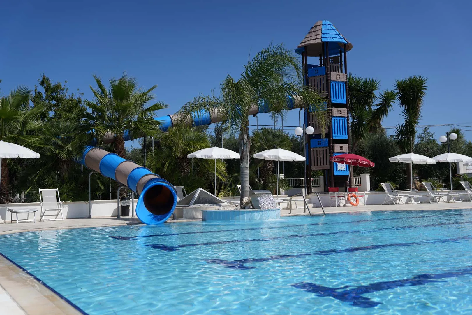 Scivolo acquatico blu con torre di gioco tra le palme a bordo piscina