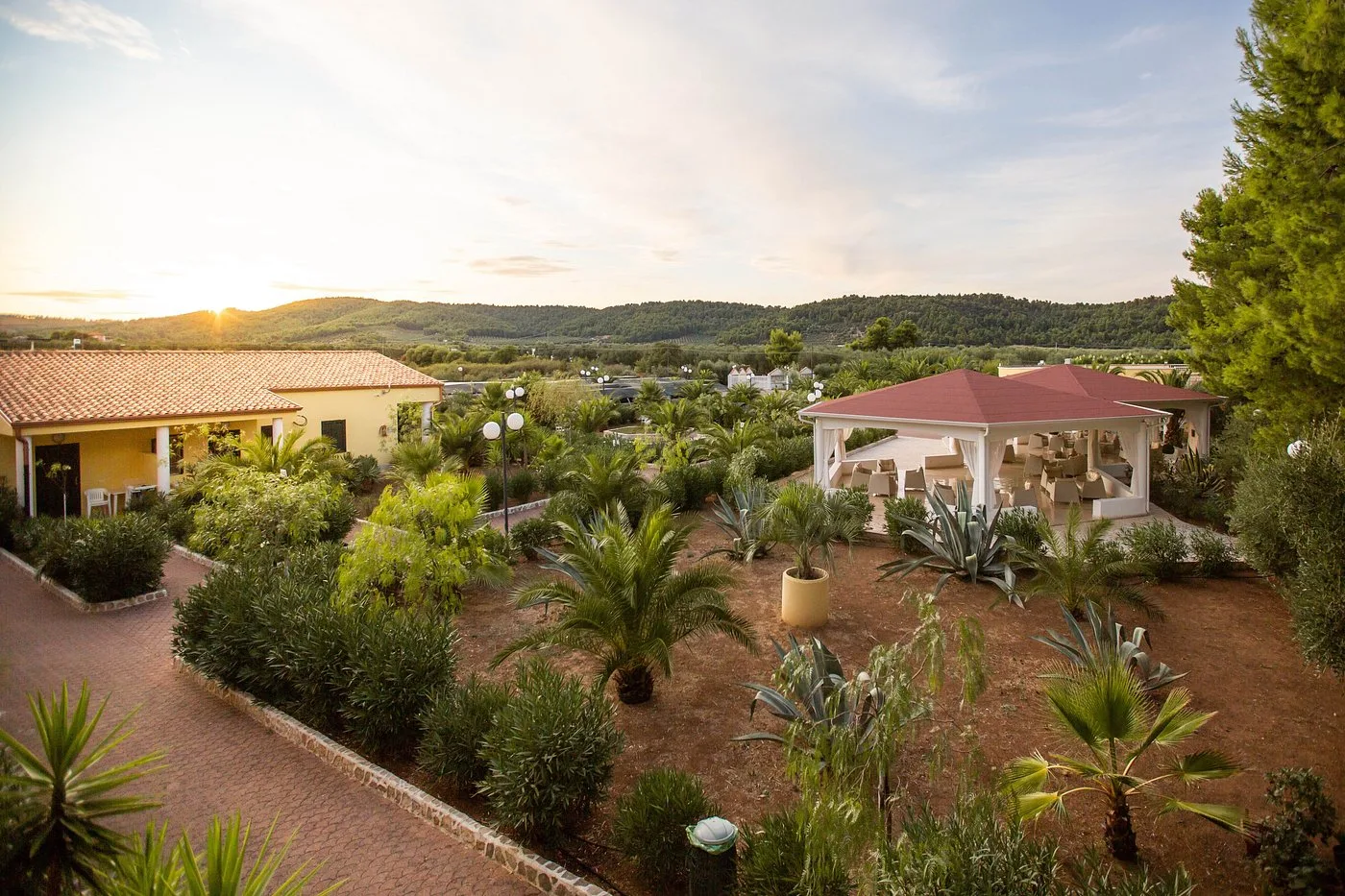 Giardino curato con palme e gazebo al tramonto tra le colline