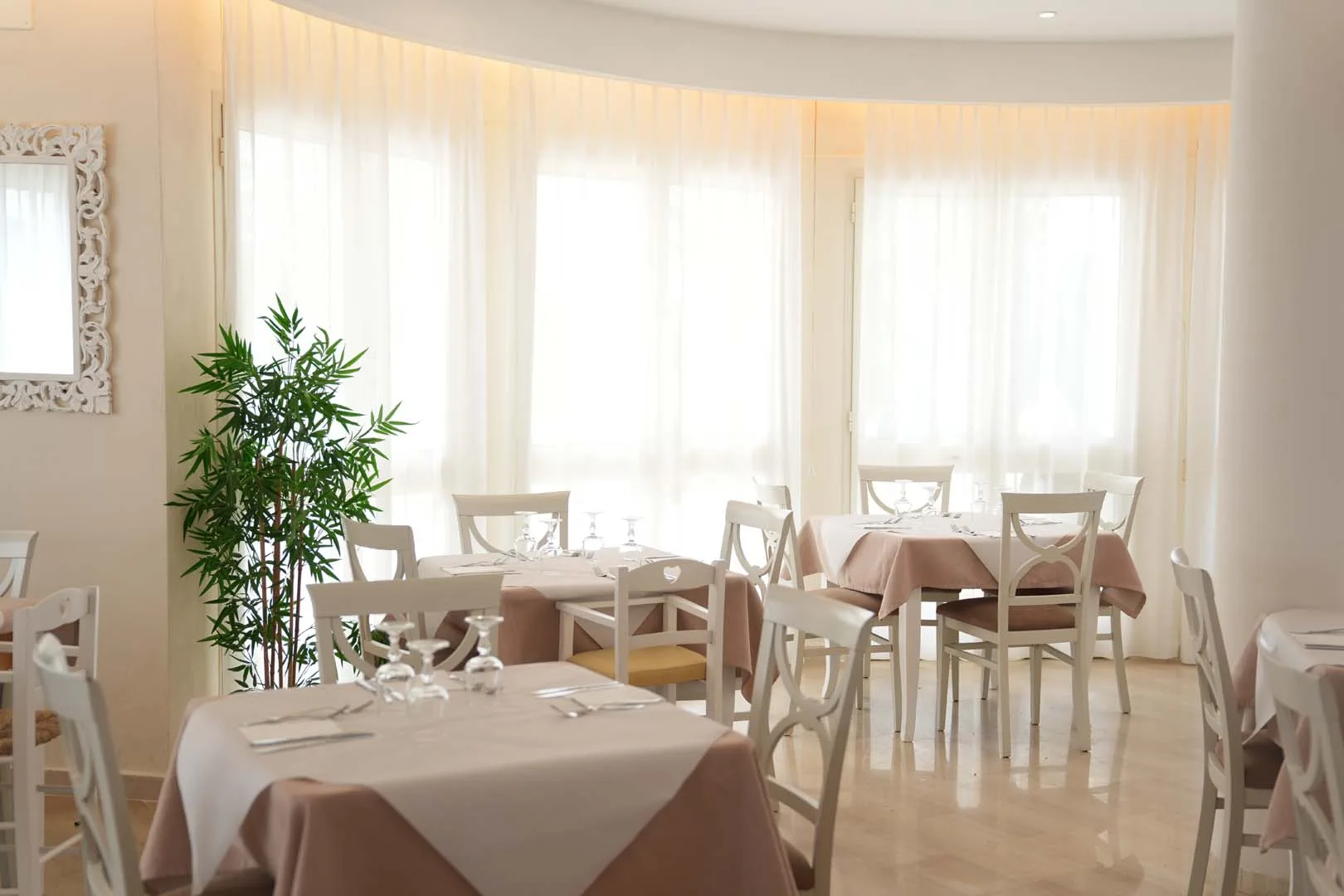 Angolo del ristorante con tavoli apparecchiati e tende chiare alle finestre