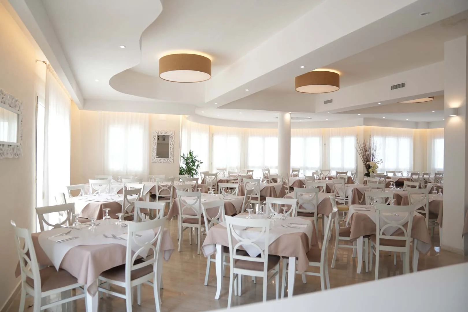 Ampia sala ristorante luminosa con tavoli bianchi e grandi finestre