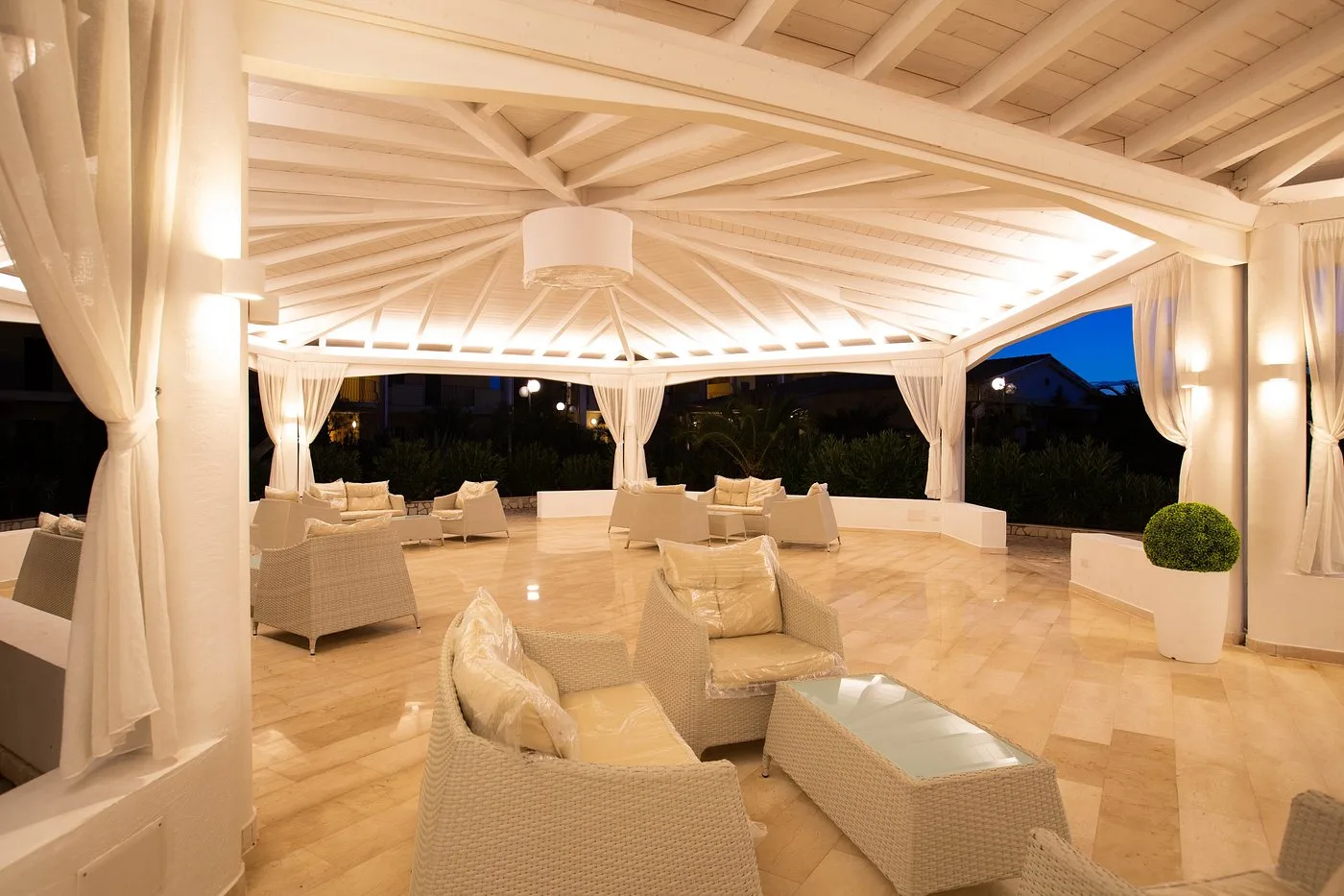 Gazebo lounge con divani bianchi in vimini illuminato di sera
