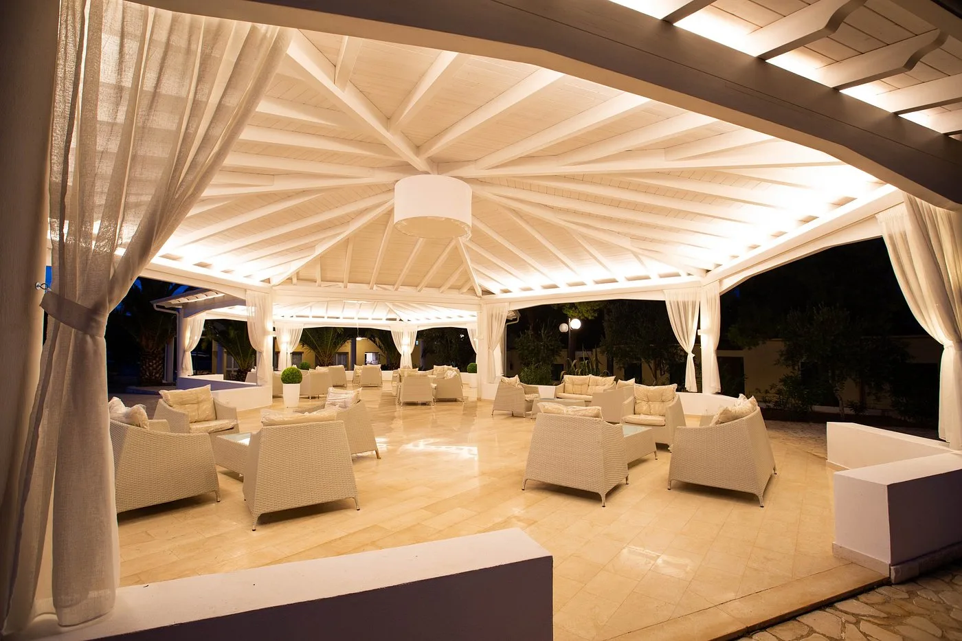 Area salotto sotto gazebo bianco con poltrone in vimini e tende chiare