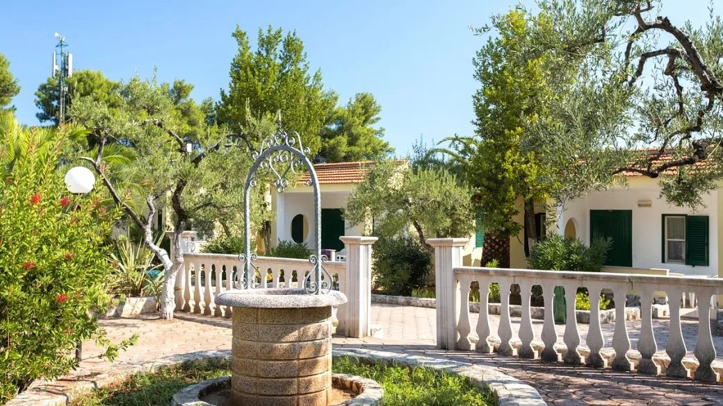 Giardino con pozzo decorativo, ulivi e villette dalle persiane verdi