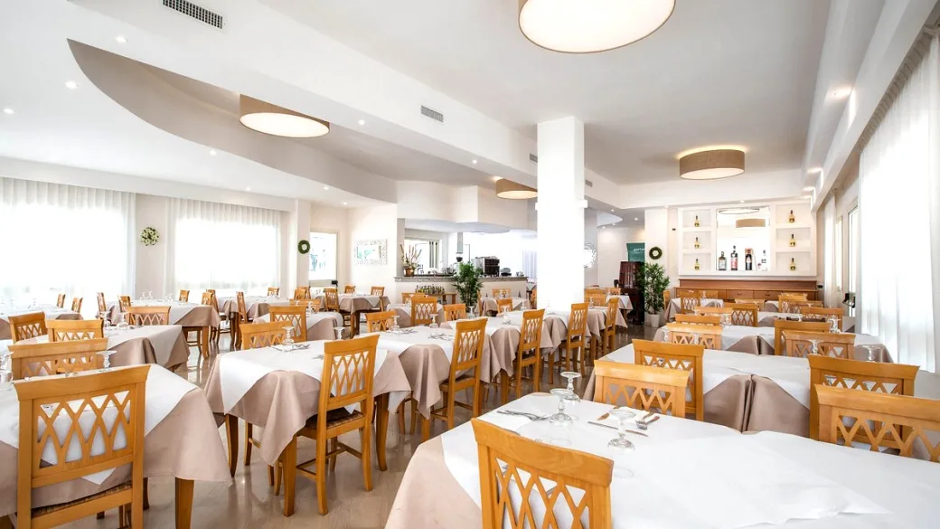 Sala ristorante luminosa con tavoli apparecchiati e sedie in legno chiaro