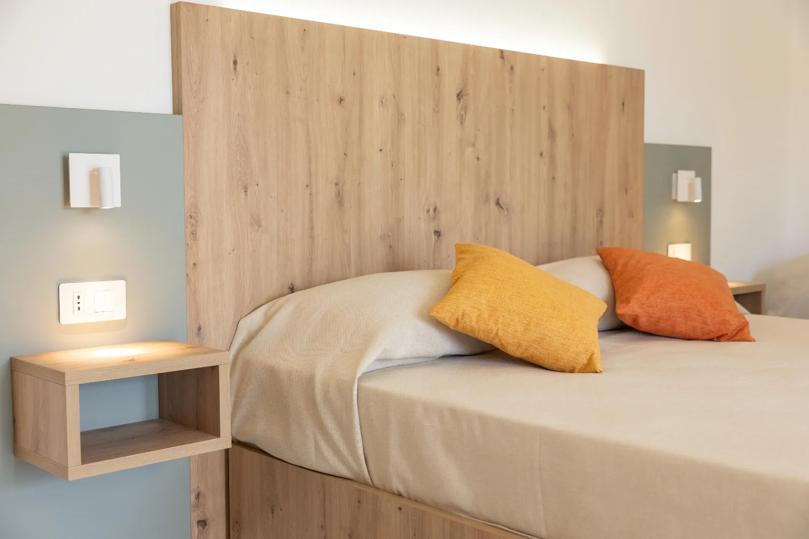 Dettaglio del letto con testiera in legno e cuscini colorati arancioni