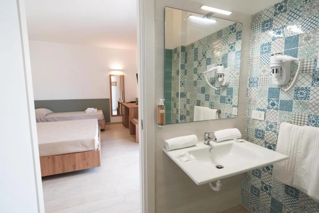 Bagno con lavabo, specchio e piastrelle decorative affacciato sulla camera