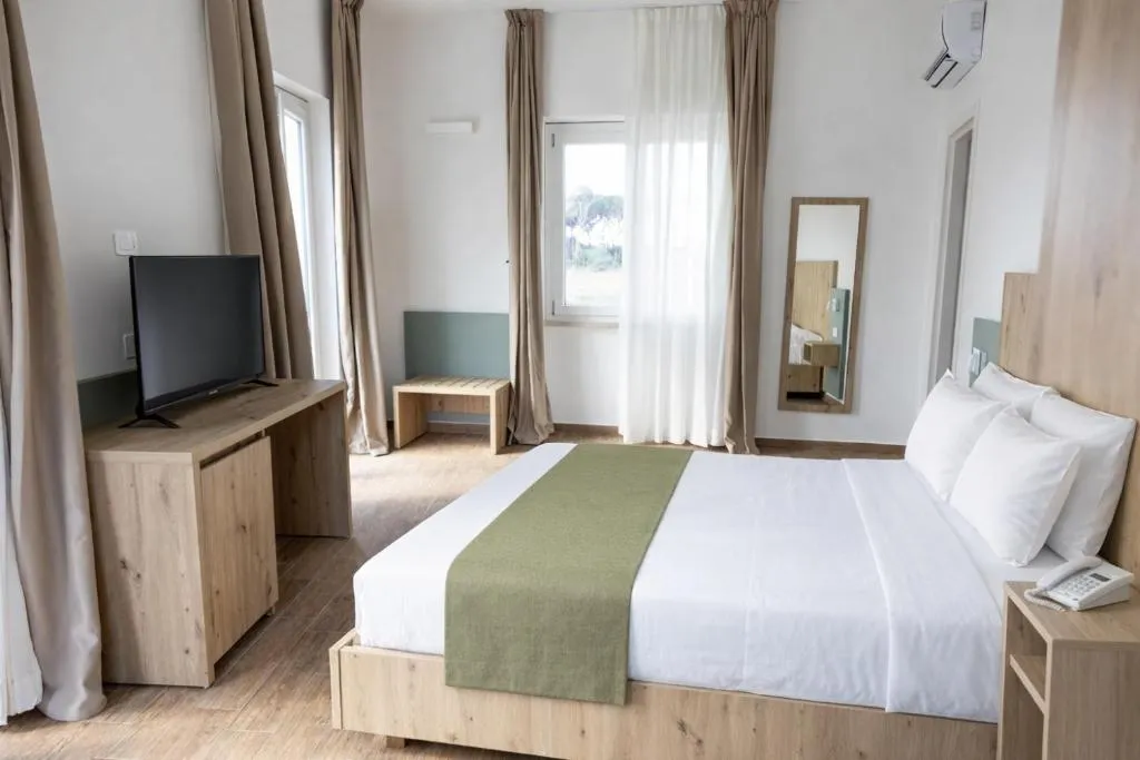 Camera matrimoniale spaziosa con letto, TV, specchio e finestre sul verde
