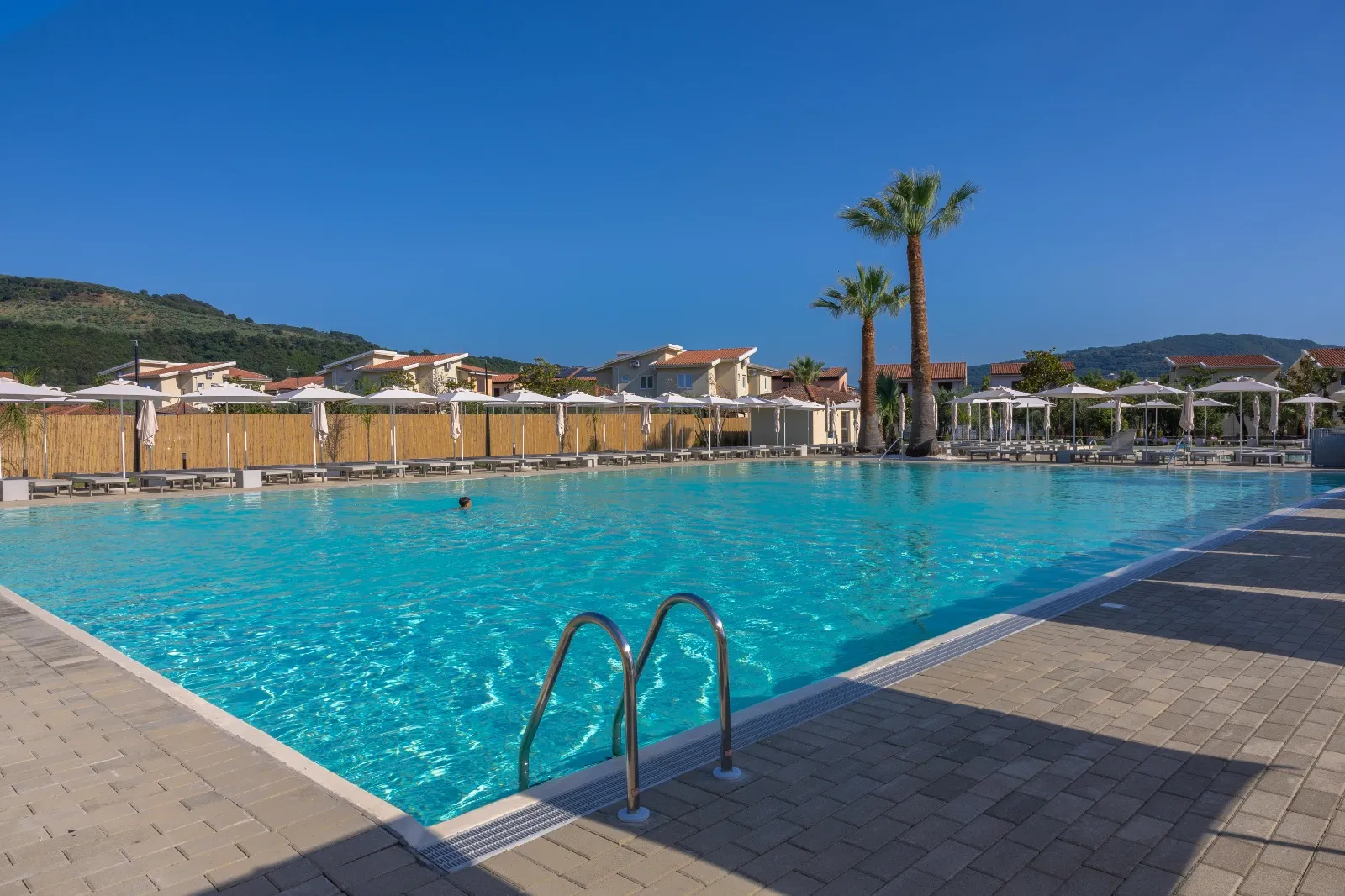 Ampia piscina del resort con palme, lettini e ombrelloni sotto il cielo azzurro