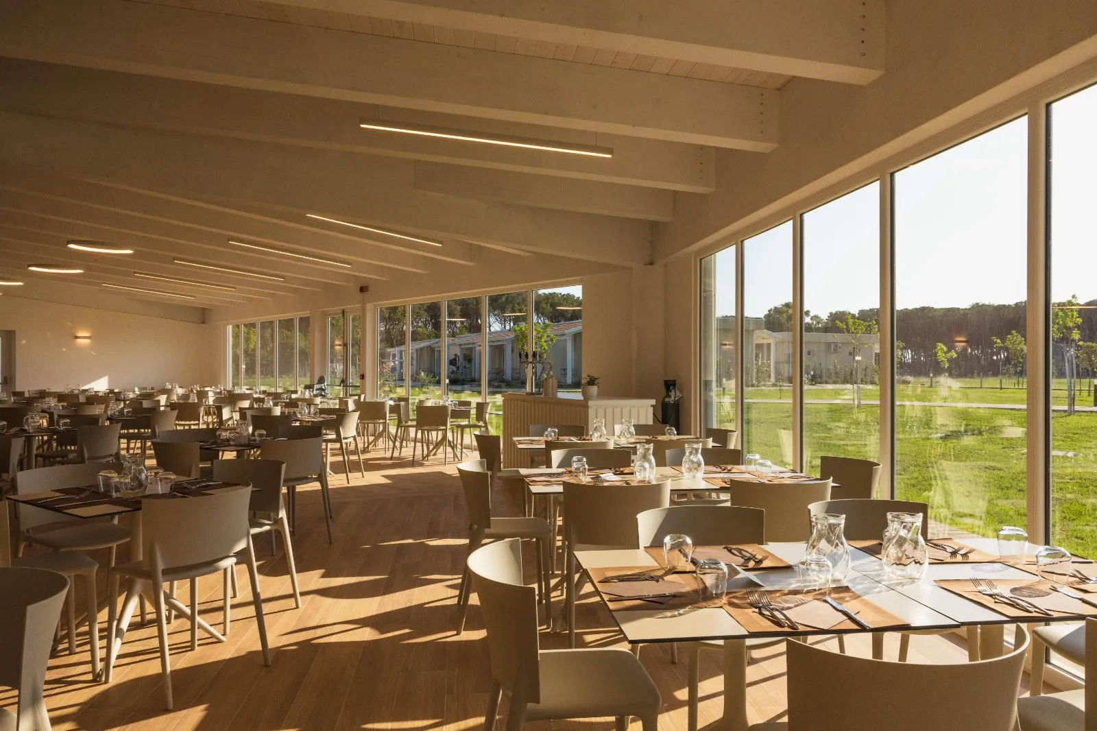 Interno luminoso del ristorante con tavoli e vista sulla pineta al tramonto