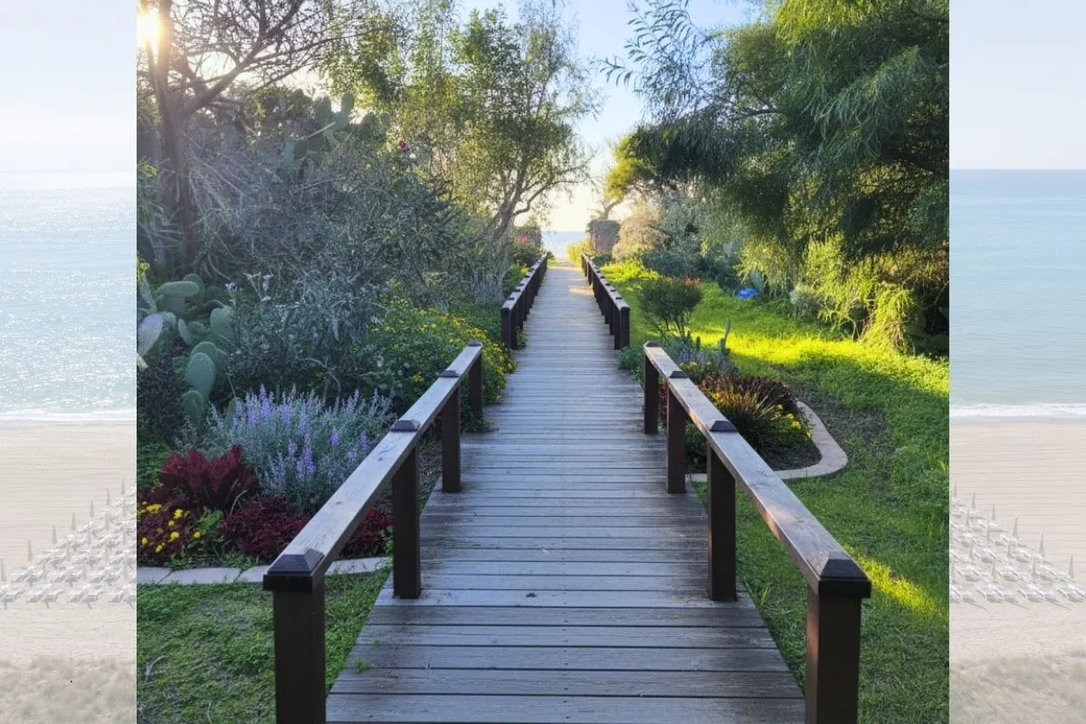 Passerella in legno tra giardini fioriti che conduce alla spiaggia e al mare