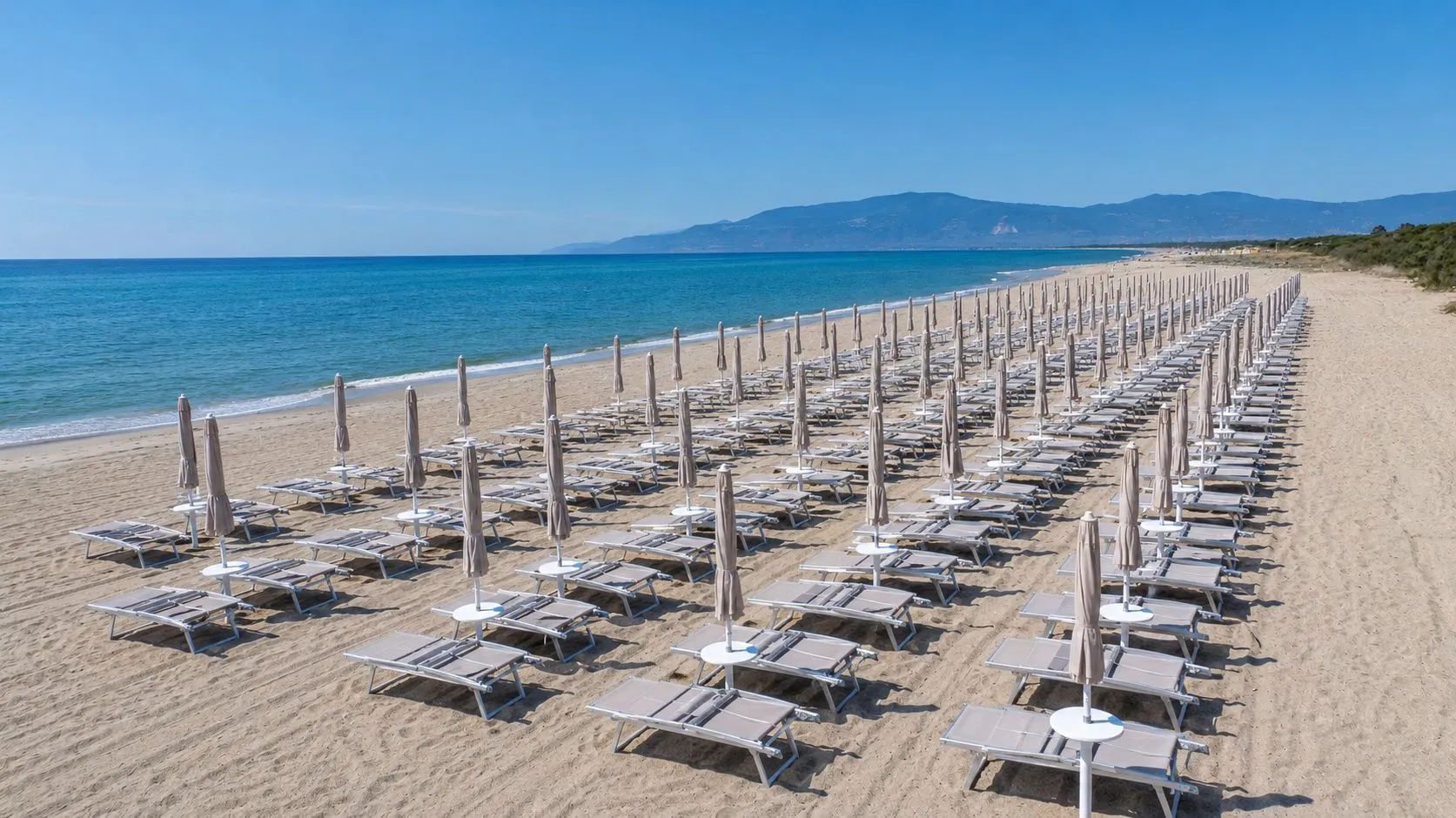Spiaggia sabbiosa con lunghe file di lettini e ombrelloni lungo la costa