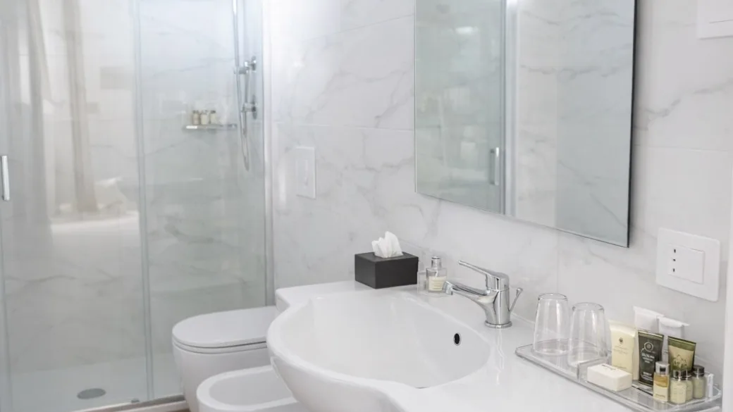Bagno moderno con doccia in vetro, lavabo e rivestimento effetto marmo