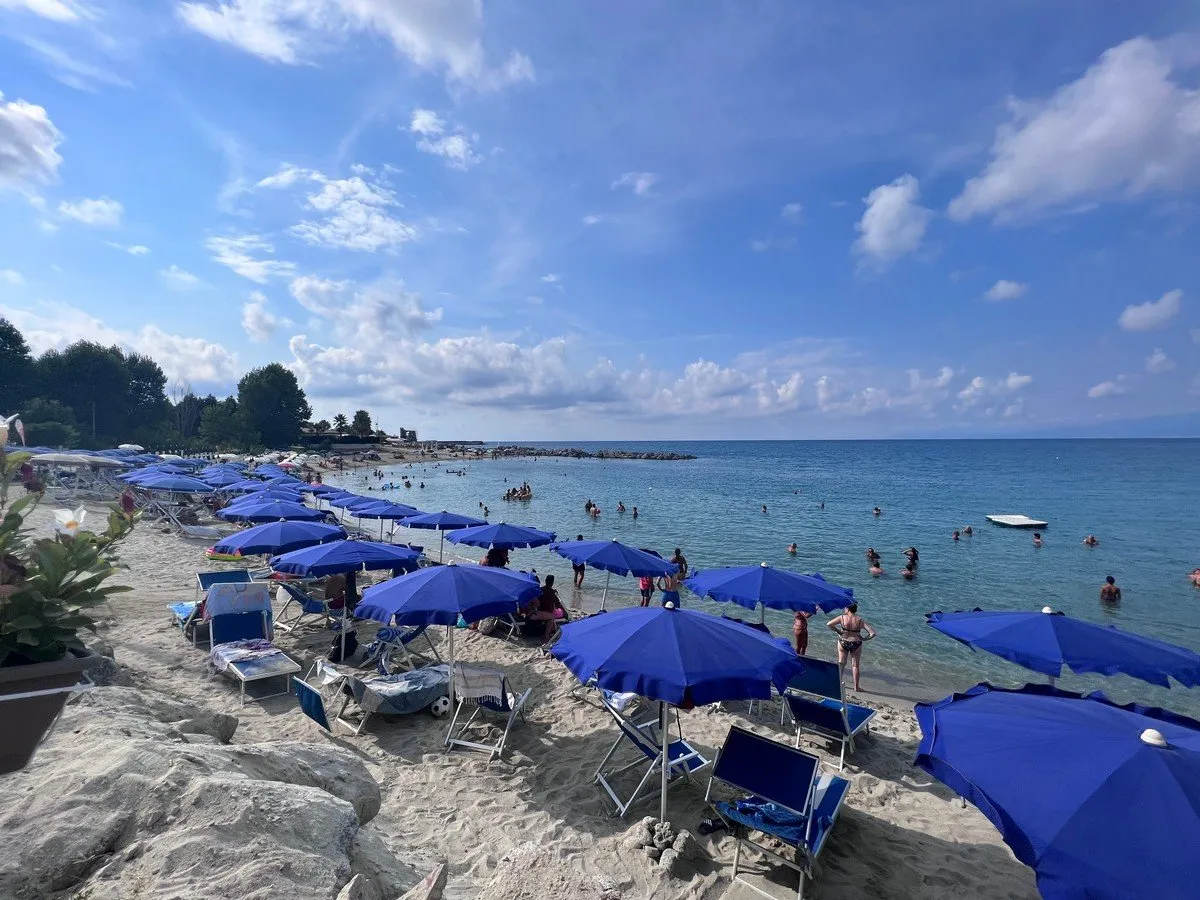 Spiaggia affollata con ombrelloni blu, bagnanti e mare turchese