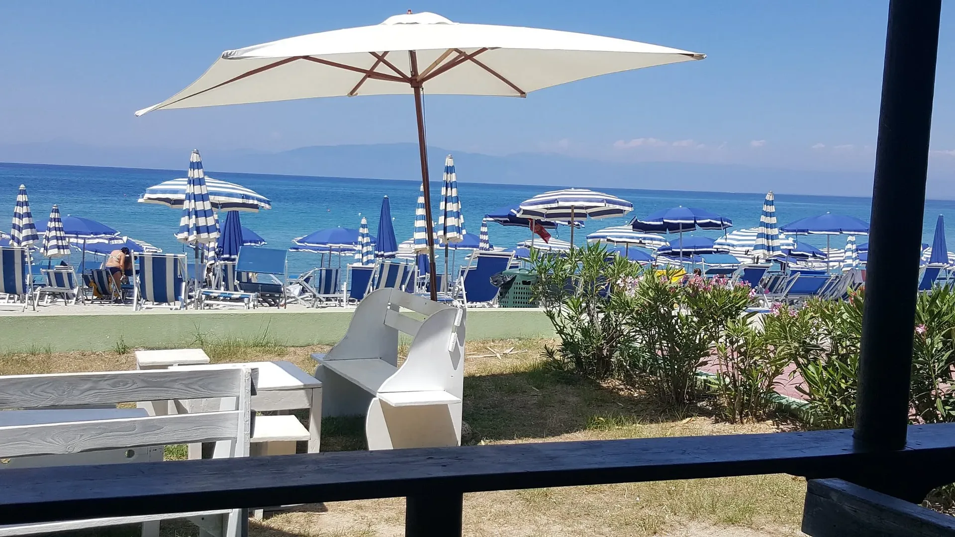 Vista sulla spiaggia con ombrelloni blu e bianchi e mare cristallino