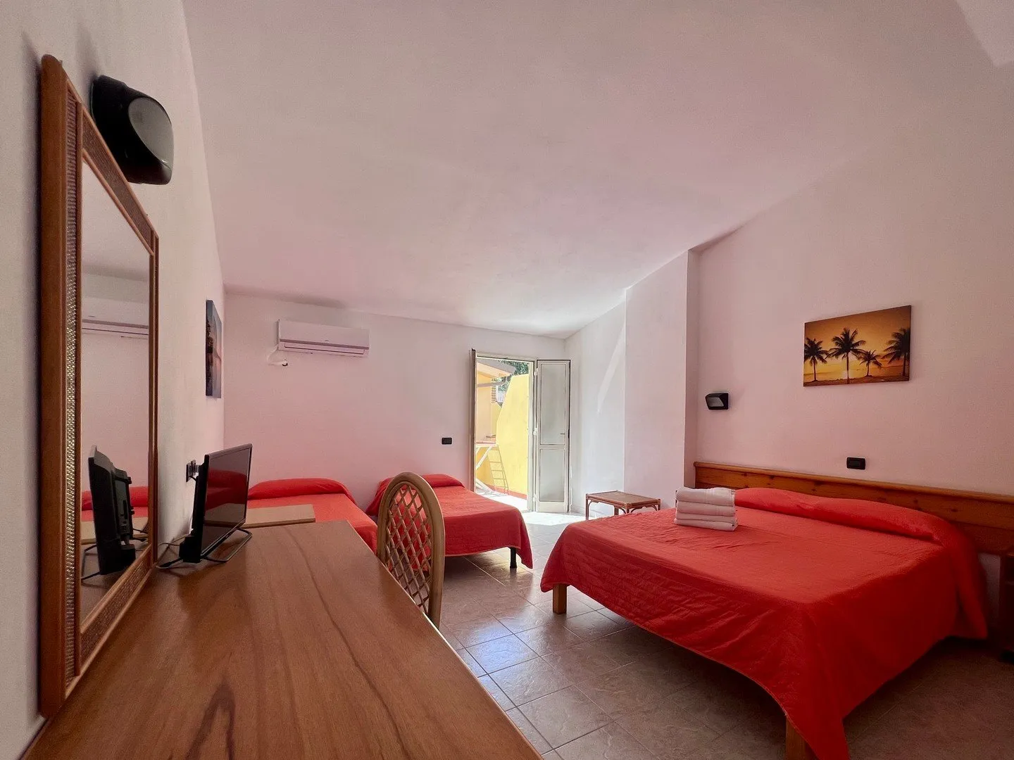 Camera con letti dal copriletto rosso, TV e uscita sul balcone
