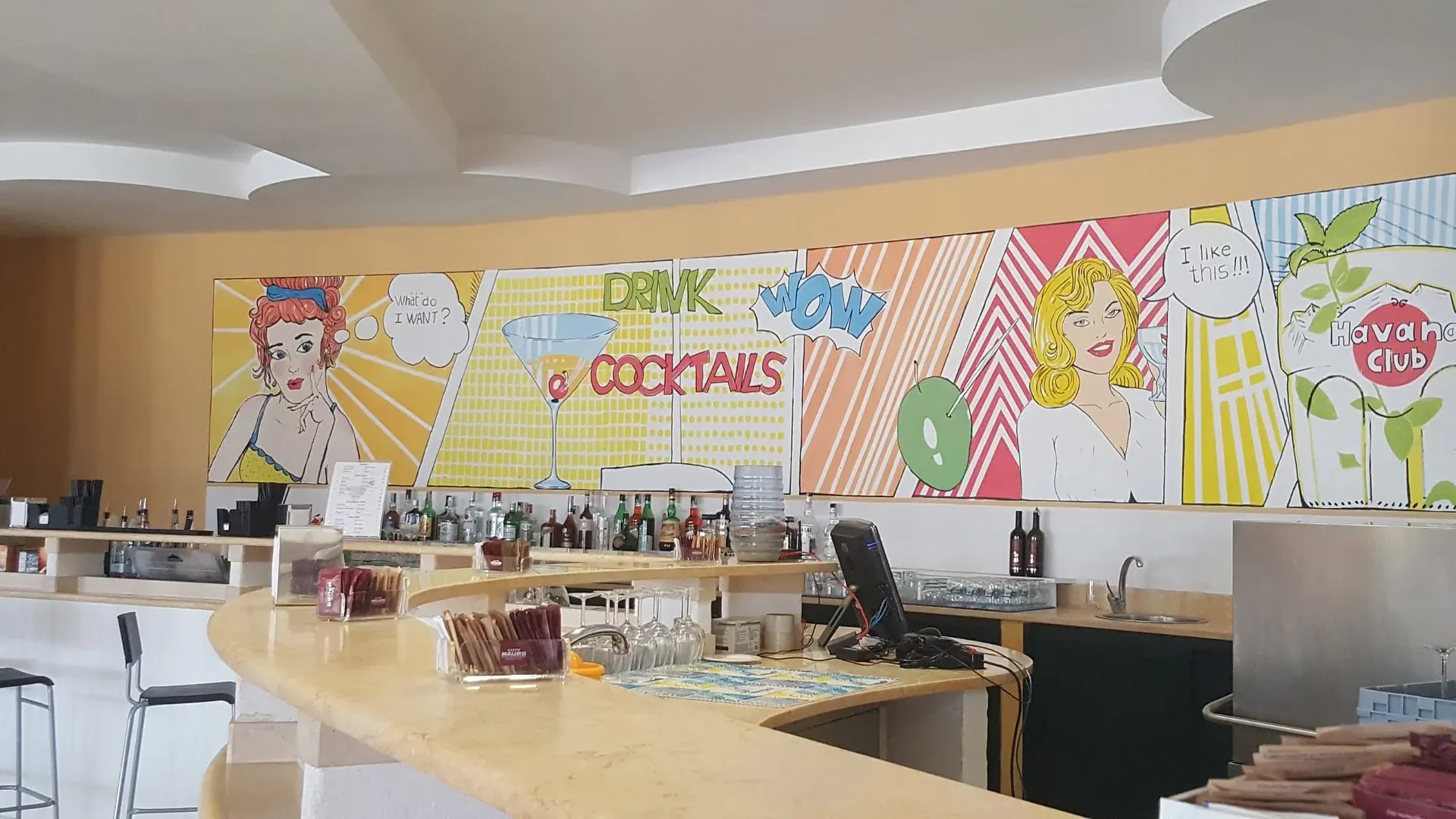 Bancone bar con murale pop art di cocktail e bottiglie esposte