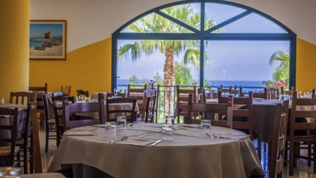 Sala ristorante con tavoli apparecchiati e grande vetrata vista mare