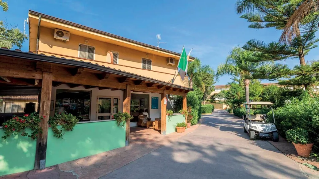 Ingresso del resort con reception, bandiera e golf cart tra la vegetazione