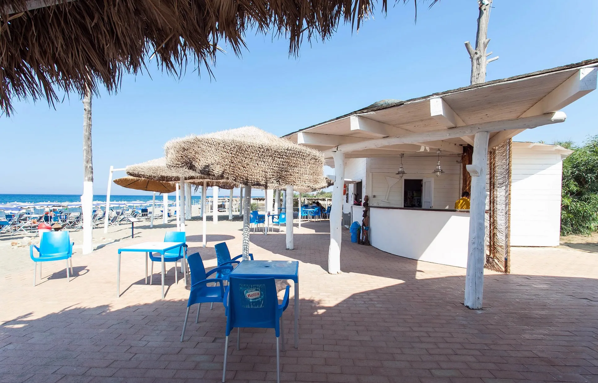 Bar sulla spiaggia con capanna in legno, ombrelloni in paglia e vista sul mare