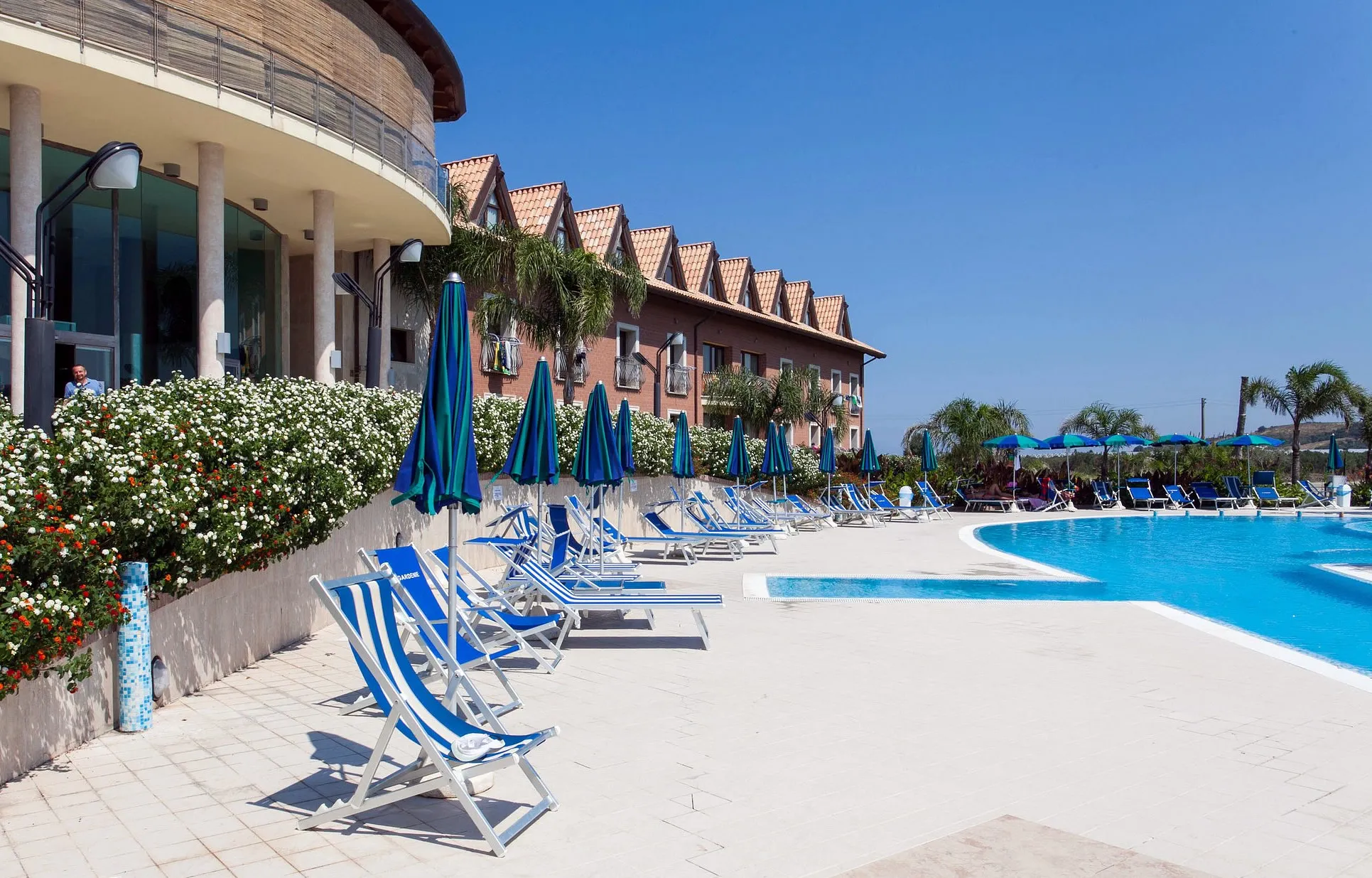 Bordo piscina con lettini e sdraio blu accanto all'edificio circolare del resort
