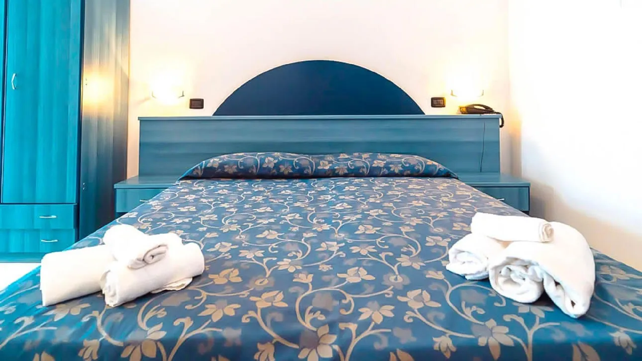 Dettaglio del letto matrimoniale con copriletto blu decorato e asciugamani