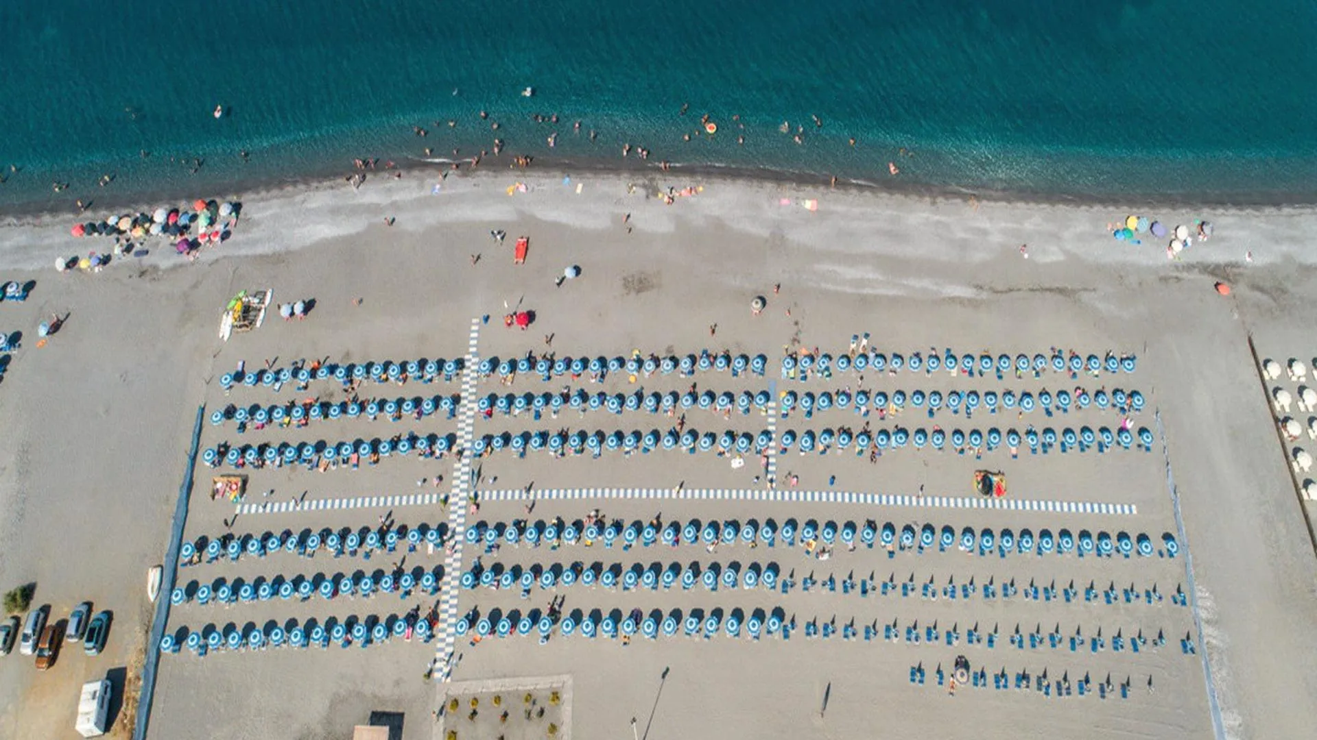 Veduta aerea della spiaggia con file ordinate di ombrelloni blu e mare