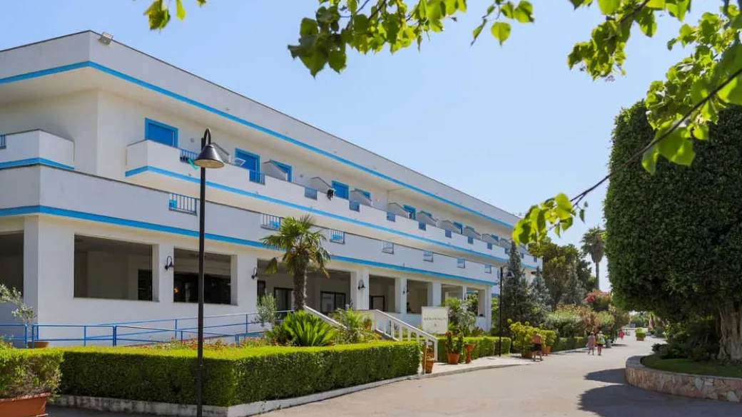 Facciata bianca e azzurra dell'hotel con balconi e giardino curato