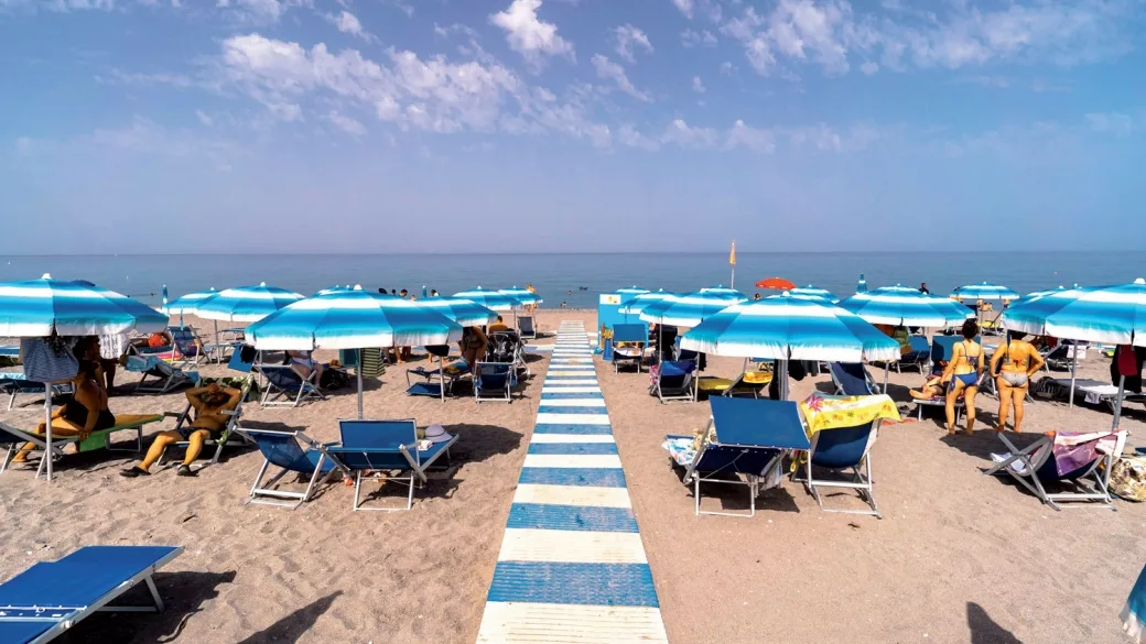 Spiaggia con ombrelloni a righe bianche e azzurre e lettini vista mare