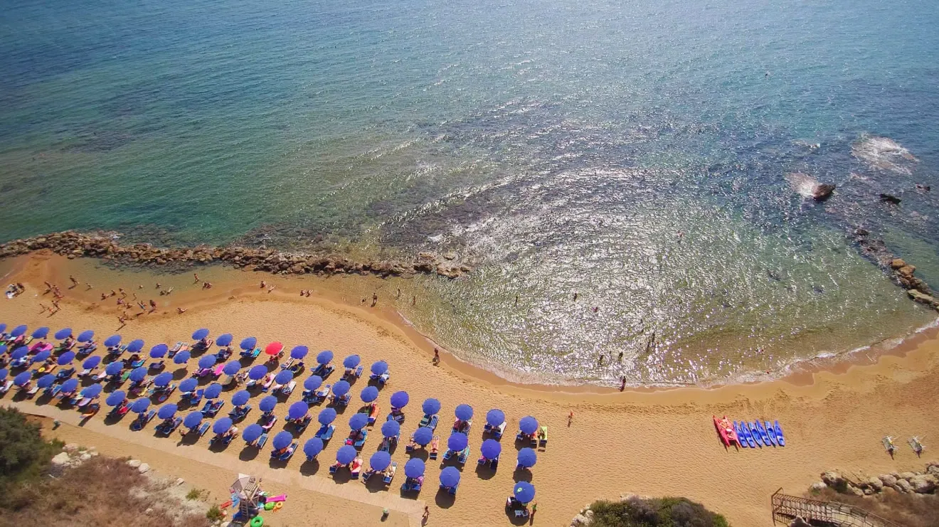 Veduta aerea della spiaggia con file di ombrelloni blu, sabbia dorata e pattini colorati