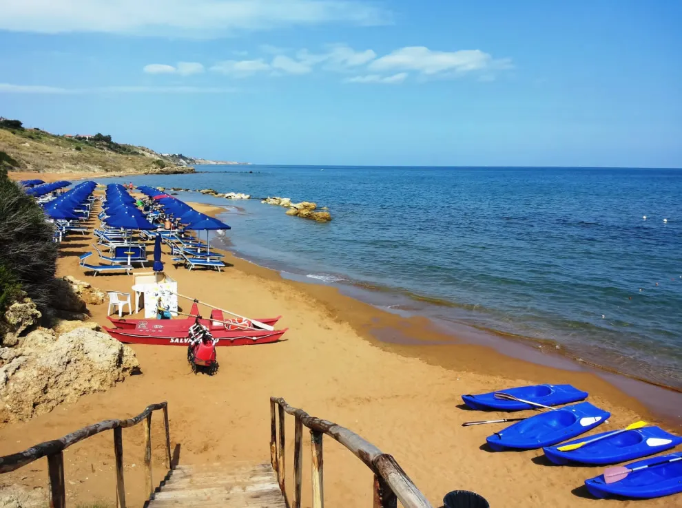 Spiaggia sabbiosa con ombrelloni blu, kayak e pattino di salvataggio in riva al mare