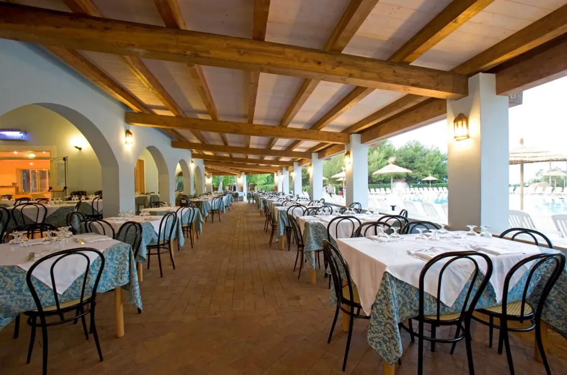 Ristorante all'aperto coperto con travi in legno, tavoli apparecchiati e vista sulla piscina
