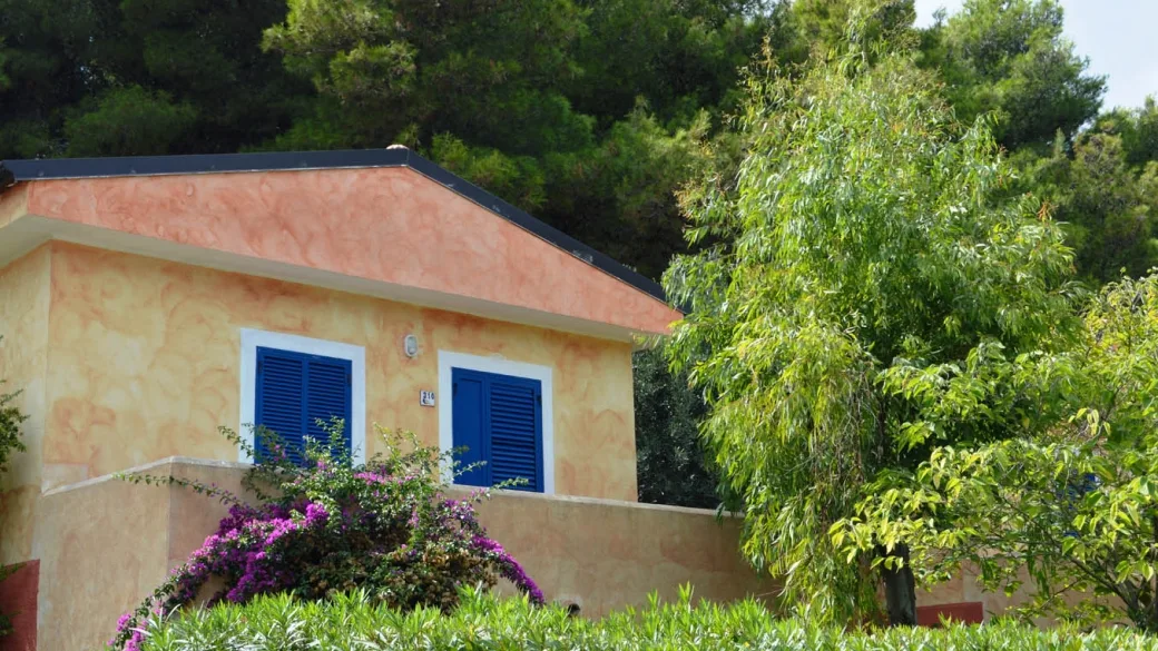 Casetta del resort color pesca con persiane blu circondata da vegetazione fiorita