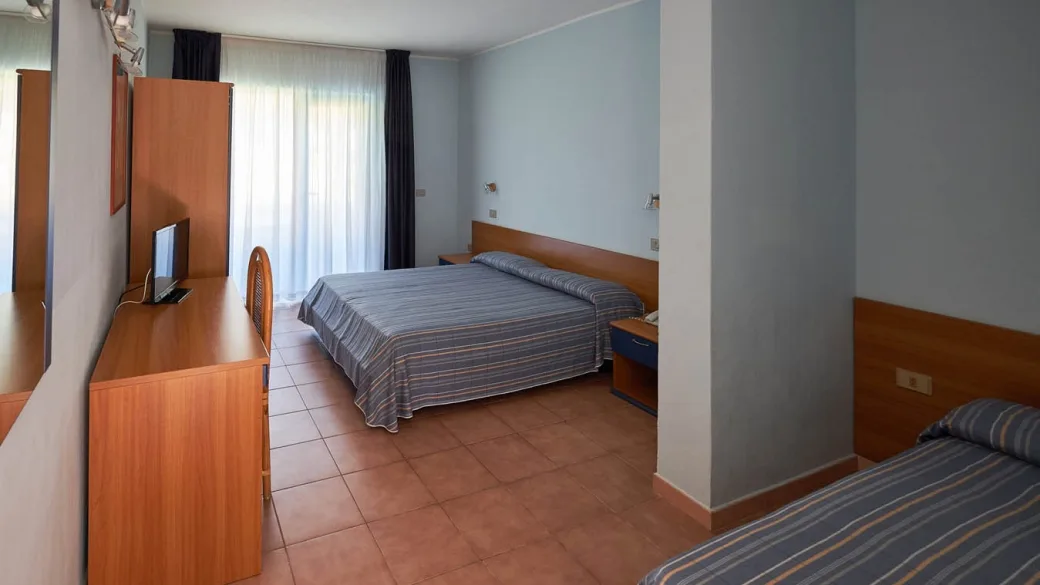 Camera con letto matrimoniale, letto singolo, TV e mobili in legno con tende chiare