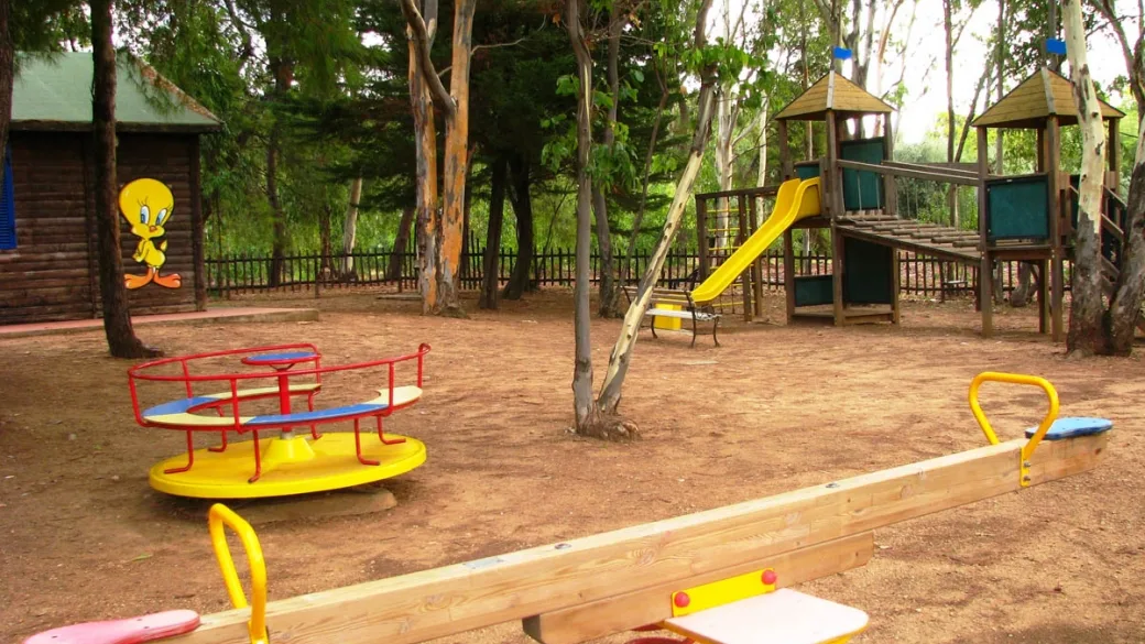 Area giochi per bambini nel bosco con giostrina, altalena a bilico e scivolo