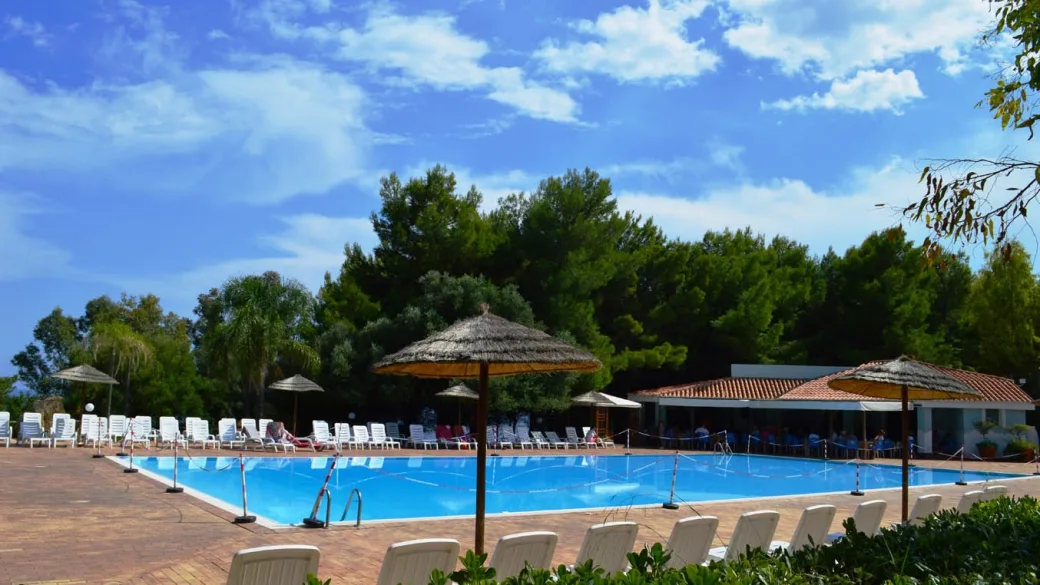 Piscina del resort con ombrelloni in paglia, lettini bianchi e bar all'aperto tra la vegetazione