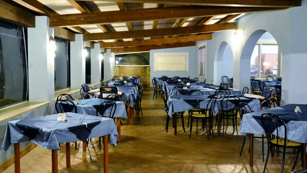 Sala ristorante interna con tavoli apparecchiati con tovaglie blu e soffitto in travi di legno